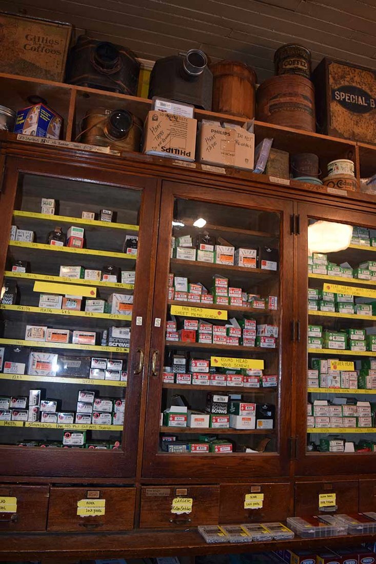 Fasteners can be found behind glass doors in century-old wooden cabinets, with antiques on display above. 