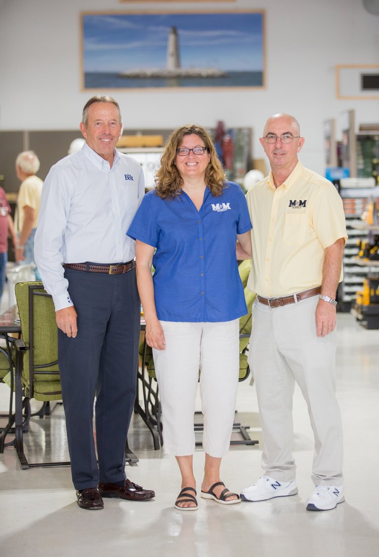 Bob Taylor, Do it Best president emeritus (left), was on hand to join owners Kathryn Tatterson and Sterling Hudgins for the grand opening of M&M Building Supply’s third store. On the back wall is a historical painting of the New Point Comfort Lighthouse, the third-oldest surviving light on the bay.